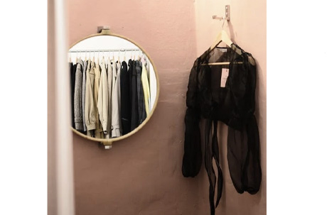 Interior of minimalistic room with lamp on wall and mirror with reflection of different clothes near blouse on hanger
